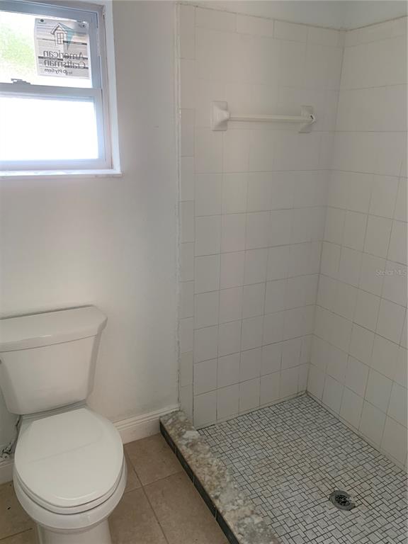 A bathroom features a white toilet next to a tiled walk-in shower — 7014 HERSHEY WAY, ORLANDO, FL