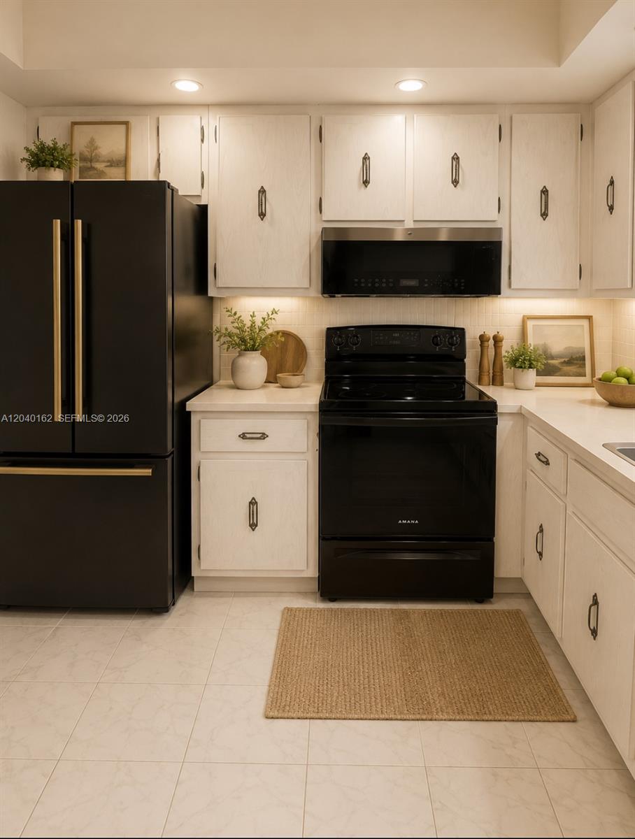 A kitchen features white cabinets, black appliances, gold hardware, and light-colored tile flooring — 600 Three Islands Blvd # 1015, Hallandale Beach FL 33009, HALLANDALE BEACH, FL