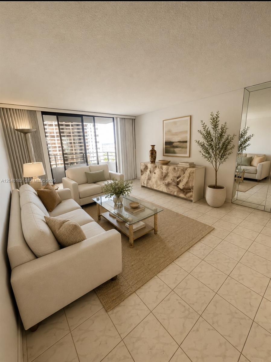A living room features two white sofas, a glass coffee table, and a large mirror — 600 Three Islands Blvd # 1015, Hallandale Beach FL 33009, HALLANDALE BEACH, FL