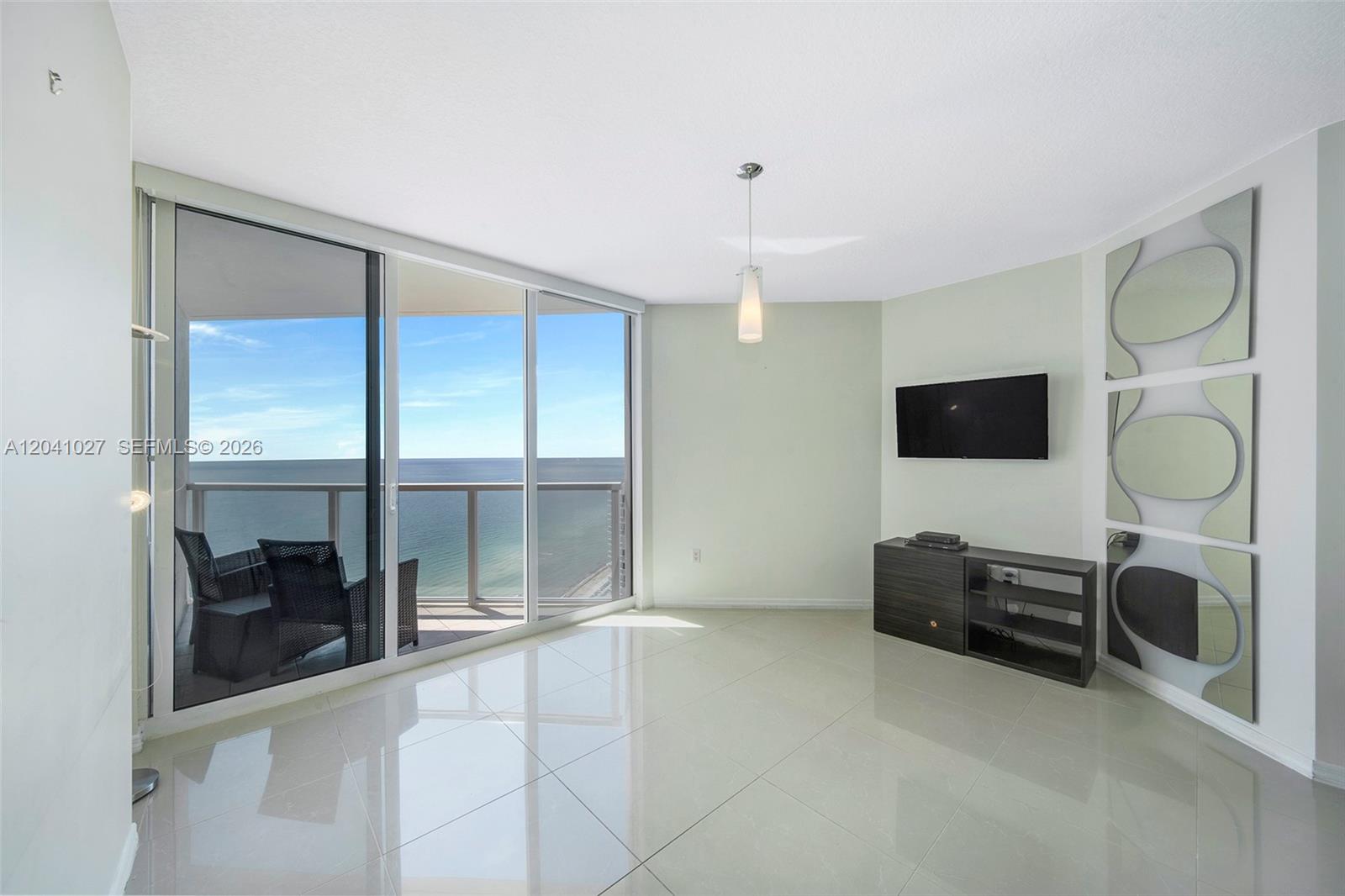 A living room with tile floors, a wall-mounted television, and a balcony overlooking the ocean — 16699 Collins Ave # 3309, Sunny Isles Beach FL 33160, SUNNY ISLES BEACH, FL