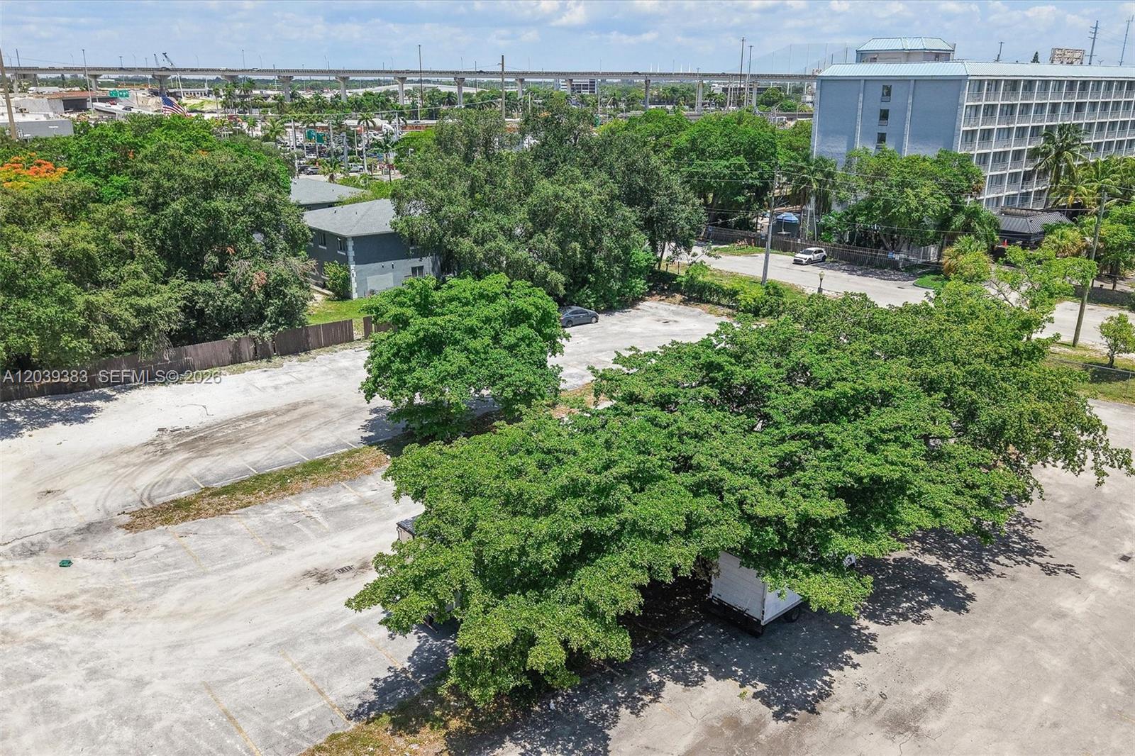 An aerial view shows a paved parking lot shaded by large trees near a building — 1st ave NW 166 st, Miami FL 33169, MIAMI, FL