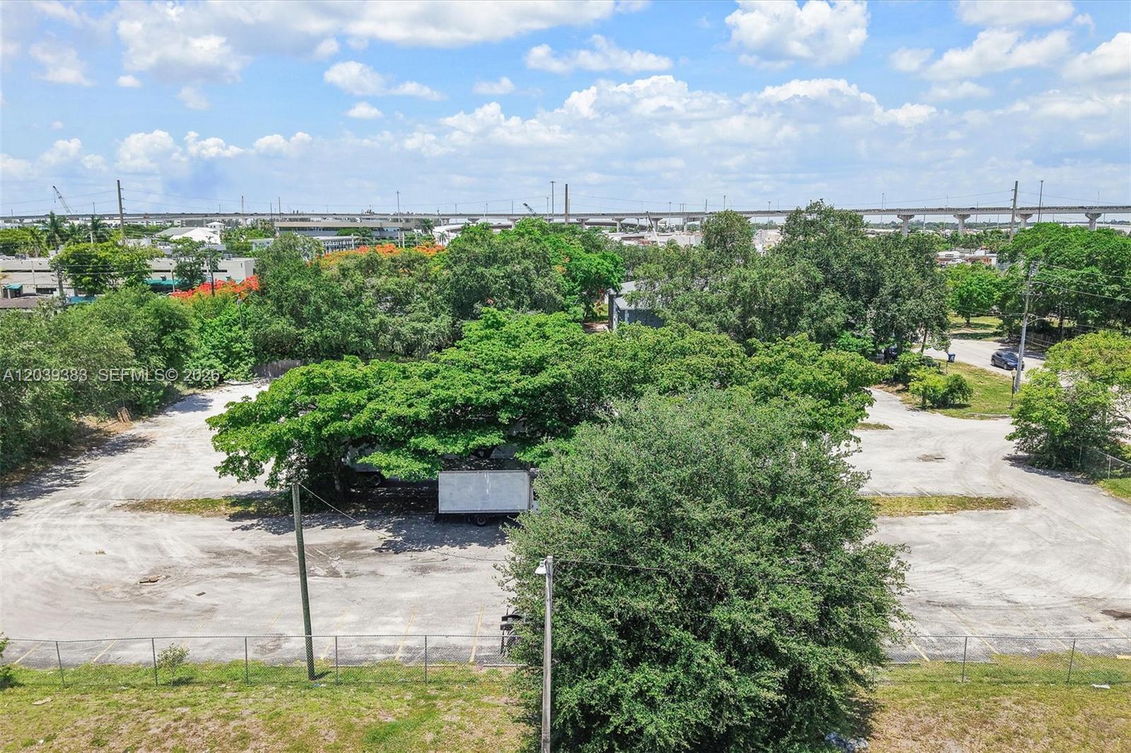 An aerial view shows a large, paved parking lot surrounded by mature trees and greenery — 1st ave NW 166 st, Miami FL 33169, MIAMI, FL