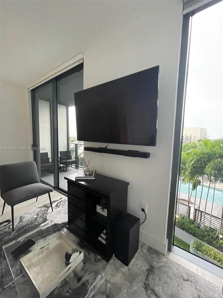 A living room features a wall-mounted television, a soundbar, a black cabinet, and a balcony — 121 NE 34th St # 1015, Miami FL 33137, MIAMI, FL