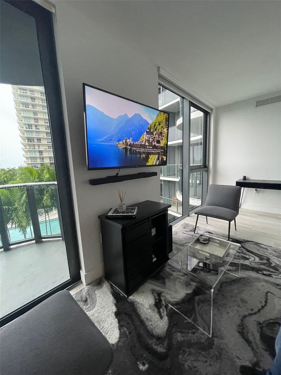 A modern living room features a wall-mounted television, a black console, and floor-to-ceiling windows — 121 NE 34th St # 1015, Miami FL 33137, MIAMI, FL