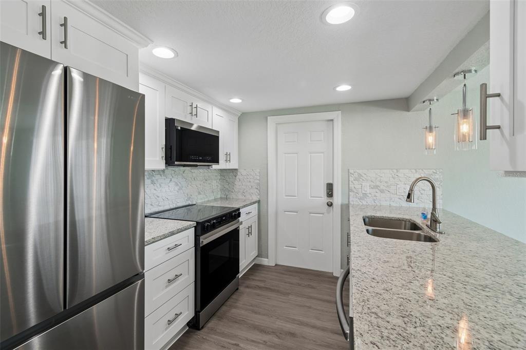 A modern kitchen features white cabinets, granite countertops, stainless steel appliances, and a marble backsplash — 4417 RUDDER WAY, NEW PORT RICHEY, FL