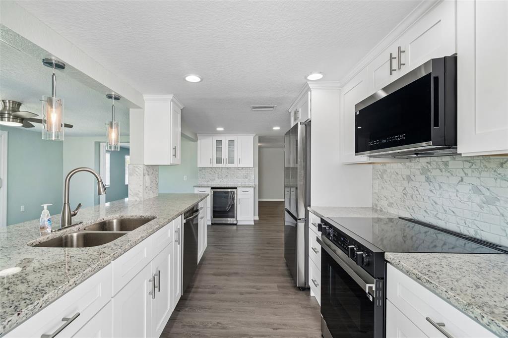 A modern kitchen features white cabinets, granite countertops, stainless steel appliances, and wood-look flooring — 4417 RUDDER WAY, NEW PORT RICHEY, FL