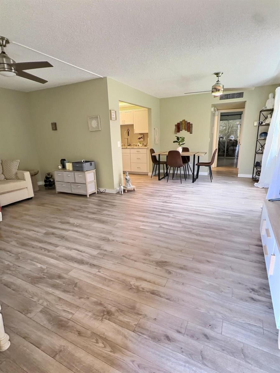 An open-concept living and dining area features light wood-look flooring and pale green walls — 199 E Burgundy E, Delray Beach FL 33484, DELRAY BEACH, FL