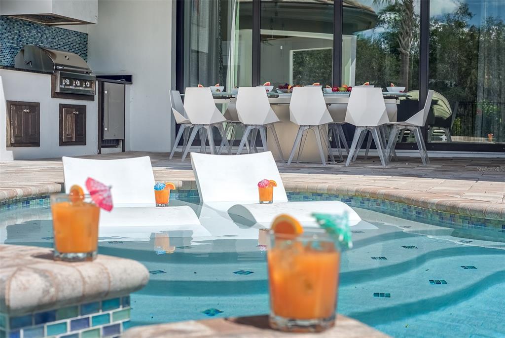 A swimming pool with lounge chairs and drinks sits in front of an outdoor dining area — 8193 VALHALLA TERRACE, REUNION, FL