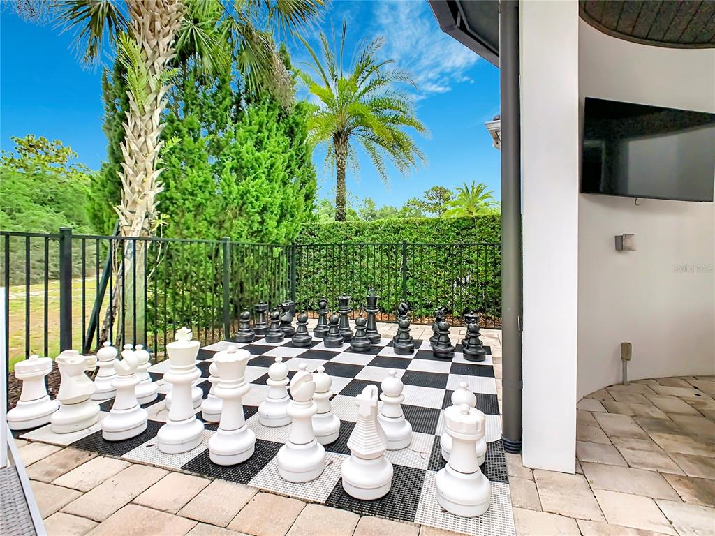 A large outdoor chessboard sits on a patio next to a black metal fence — 8193 VALHALLA TERRACE, REUNION, FL