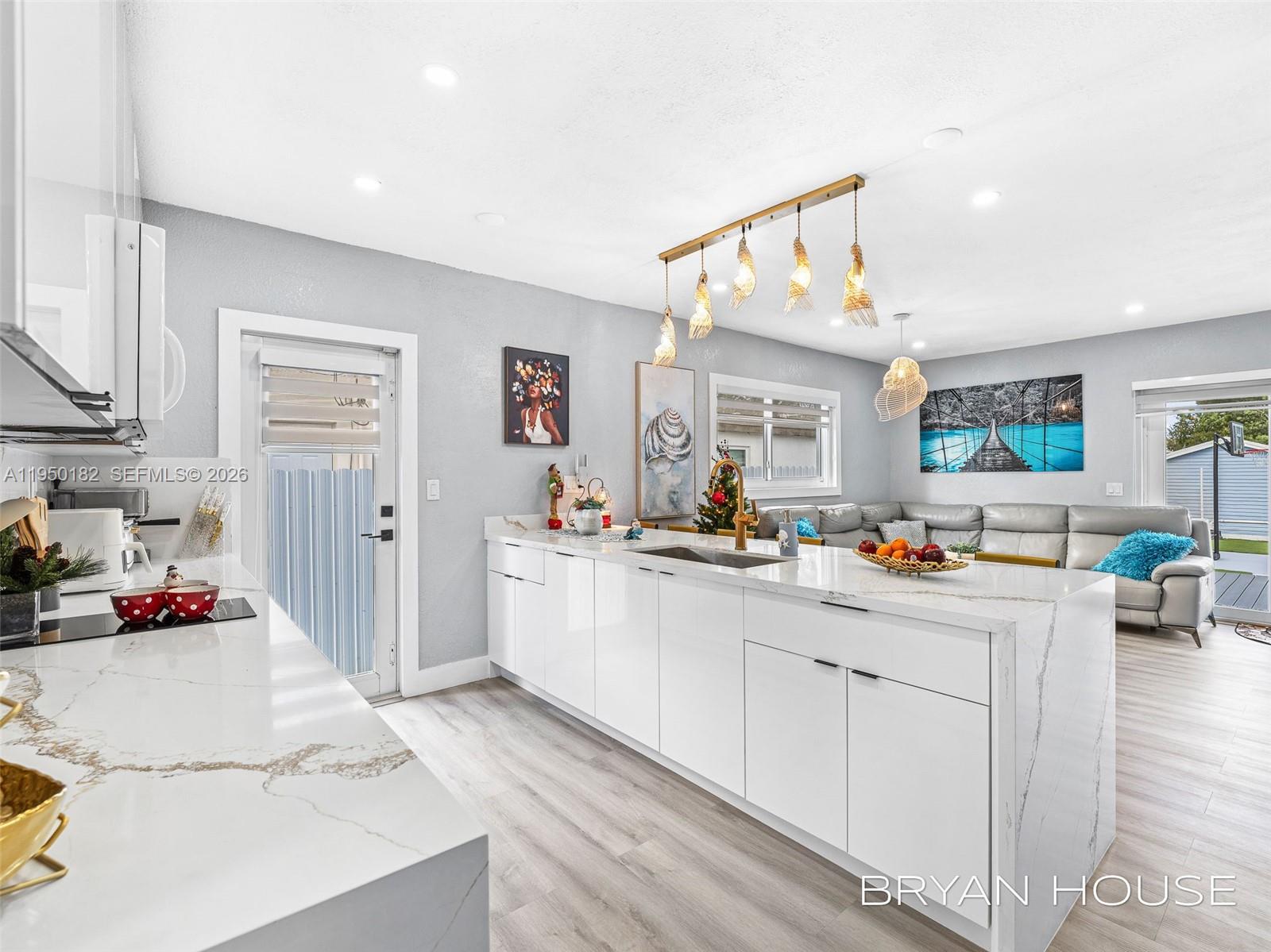 A modern kitchen features white cabinetry, a marble-topped island, and an open-concept living area — 3341 NW 20th St, Miami FL 33142, MIAMI, FL