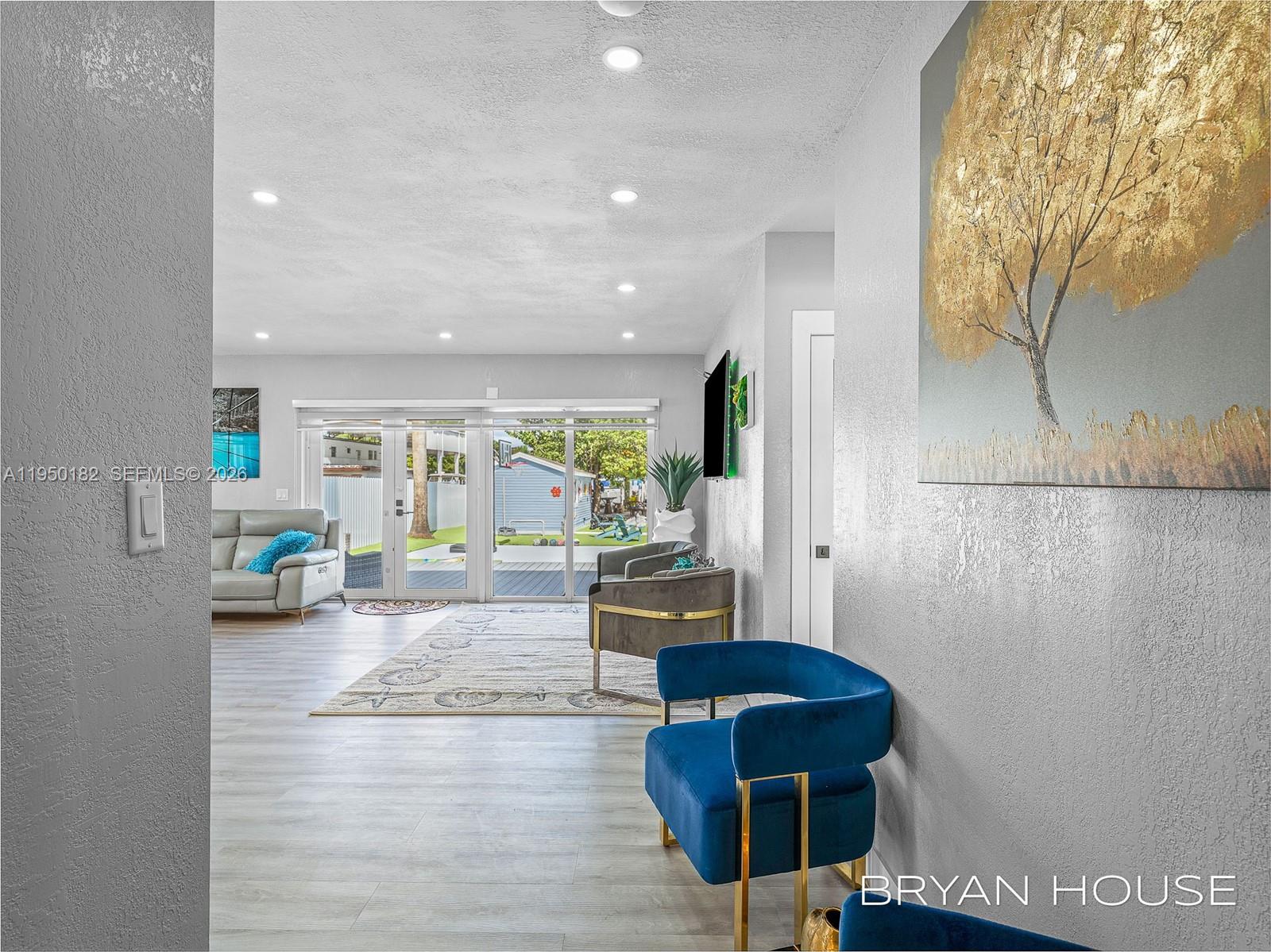 A bright living room features light wood flooring, modern blue chairs, and sliding glass doors — 3341 NW 20th St, Miami FL 33142, MIAMI, FL