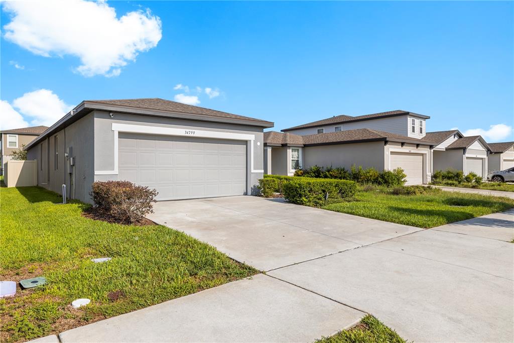 A row of suburban single-story houses with gray stucco exteriors and attached garages — 34799 TELLURIDE LANE, ZEPHYRHILLS, FL