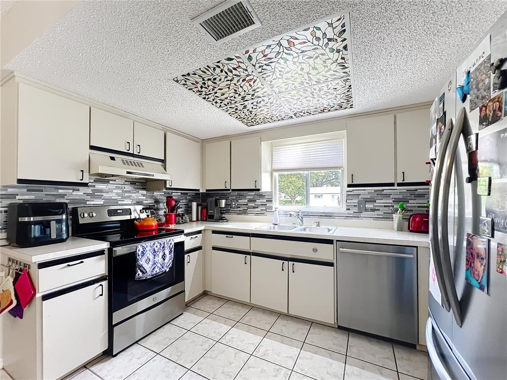 A kitchen features white cabinets, stainless steel appliances, a tiled backsplash, and a decorative ceiling panel — 6468 SW 107TH PLACE, OCALA, FL