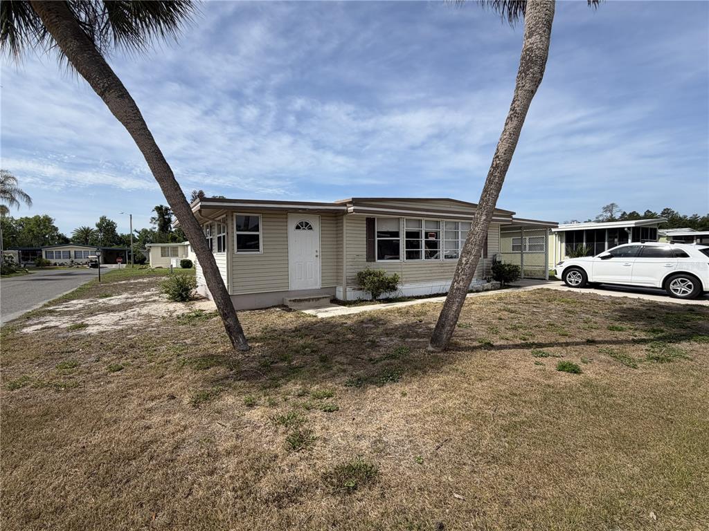 A single-story mobile home with beige siding sits on a grassy lot with palm trees — 171 PARADISE N, LEESBURG, FL