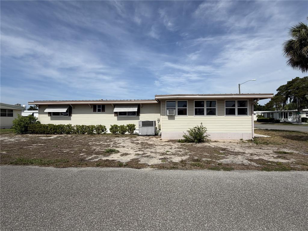 A single-story manufactured home with light-colored siding, metal awnings, and an outdoor air conditioning unit — 171 PARADISE N, LEESBURG, FL