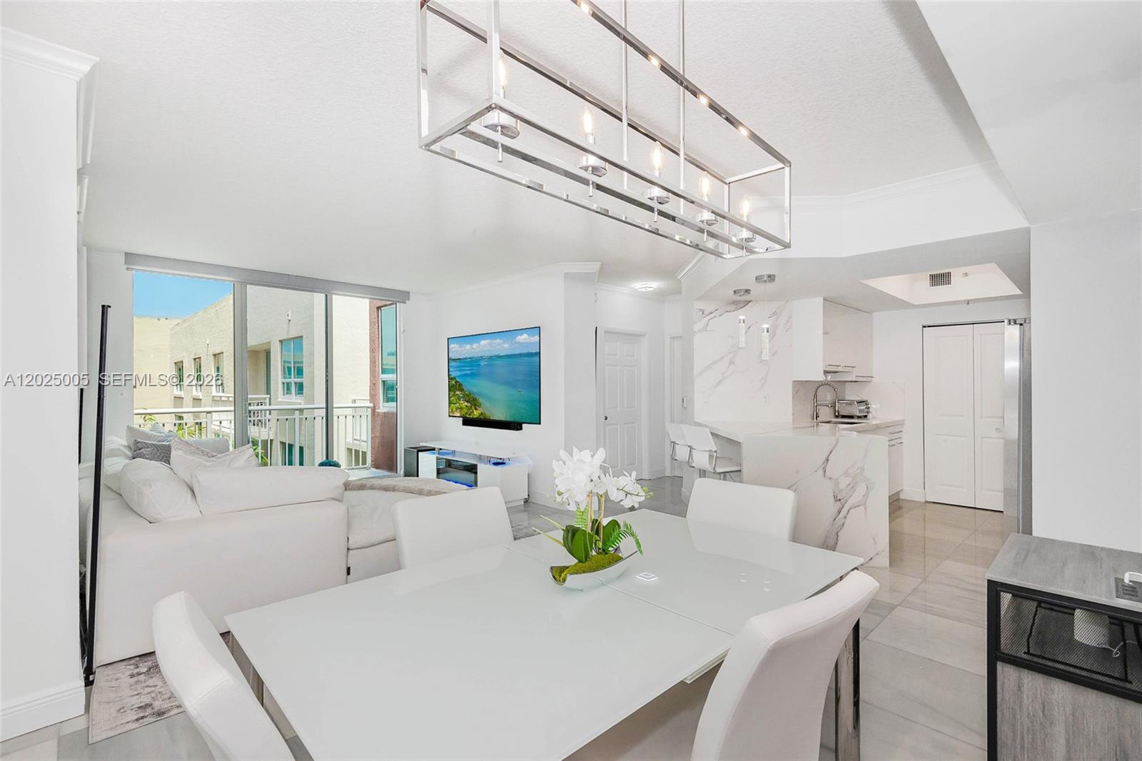A modern dining and living area features white furniture, marble accents, and a large chandelier — 2000 N Bayshore Dr # 619, Miami FL 33137, MIAMI, FL