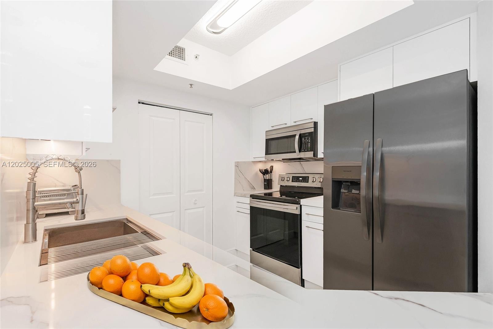 A modern kitchen features white cabinets, stainless steel appliances, and a marble-patterned countertop with fruit — 2000 N Bayshore Dr # 619, Miami FL 33137, MIAMI, FL