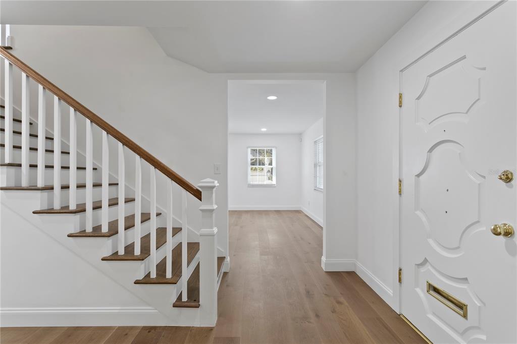 An entryway features white walls, light wood flooring, a staircase with wooden treads, and a door — 4704 W BROOKWOOD DRIVE, TAMPA, FL