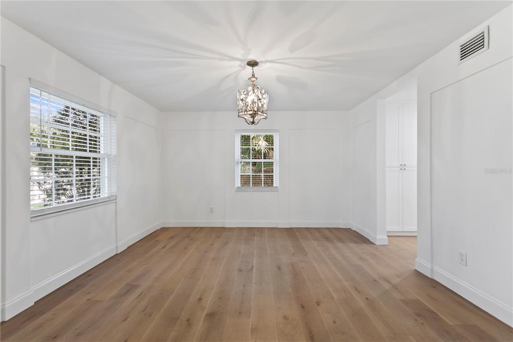 A dining room with white walls, wainscoting, a crystal chandelier, and light wood flooring — 4704 W BROOKWOOD DRIVE, TAMPA, FL