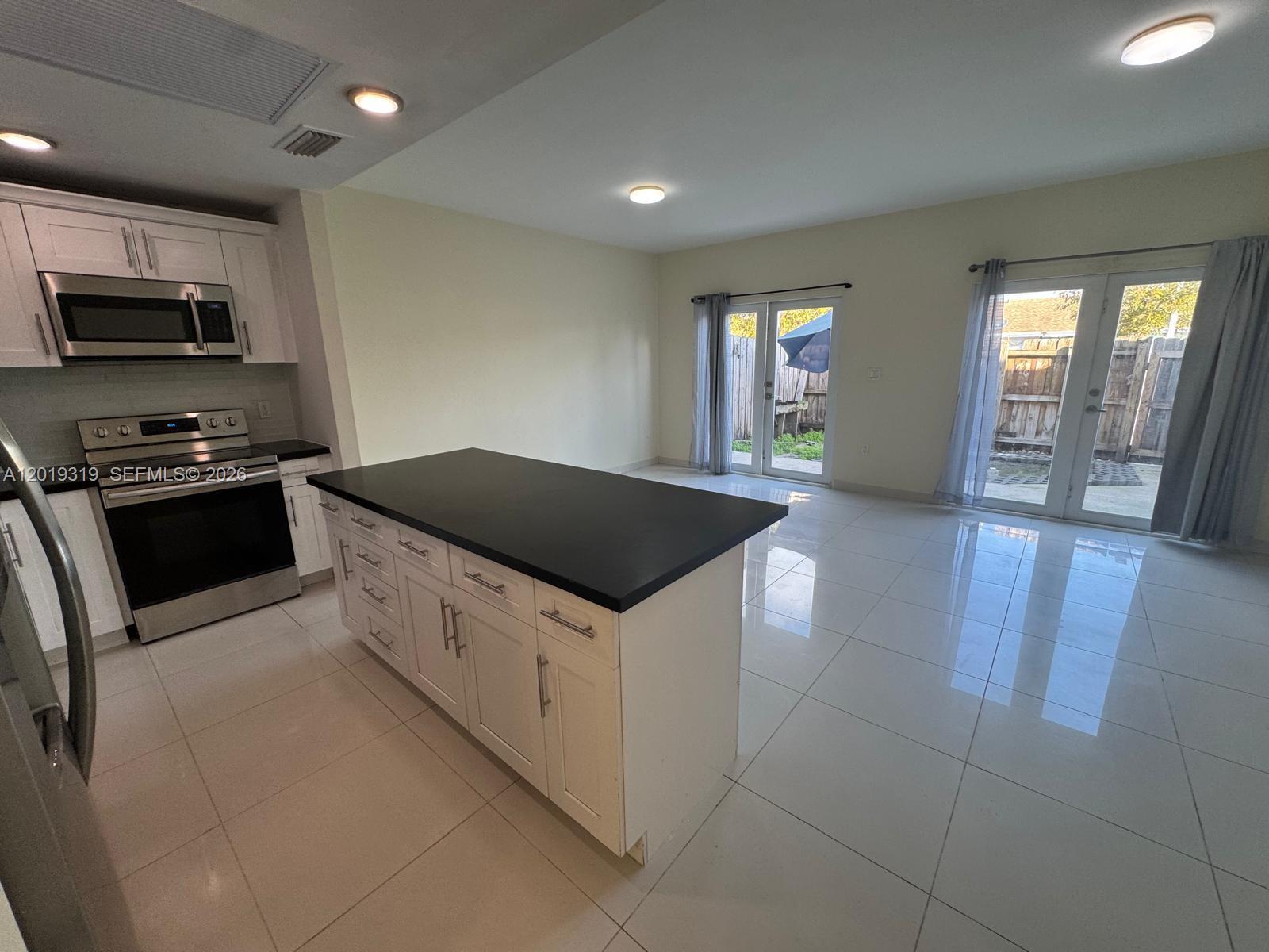 A kitchen with white cabinets, a black island, and tile floors opens to a patio — 13724 SW 259th St, Homestead FL 33032, HOMESTEAD, FL