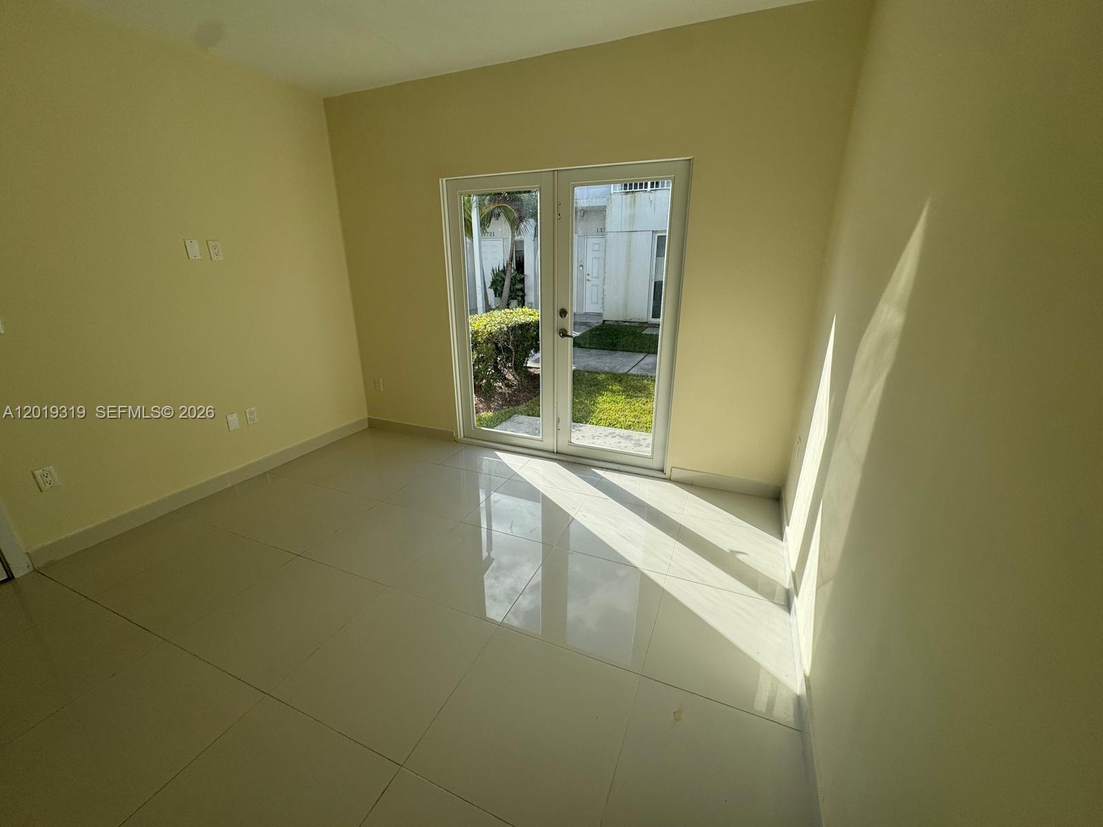 An empty room with light-colored tile floors and glass double doors leading to a patio — 13724 SW 259th St, Homestead FL 33032, HOMESTEAD, FL