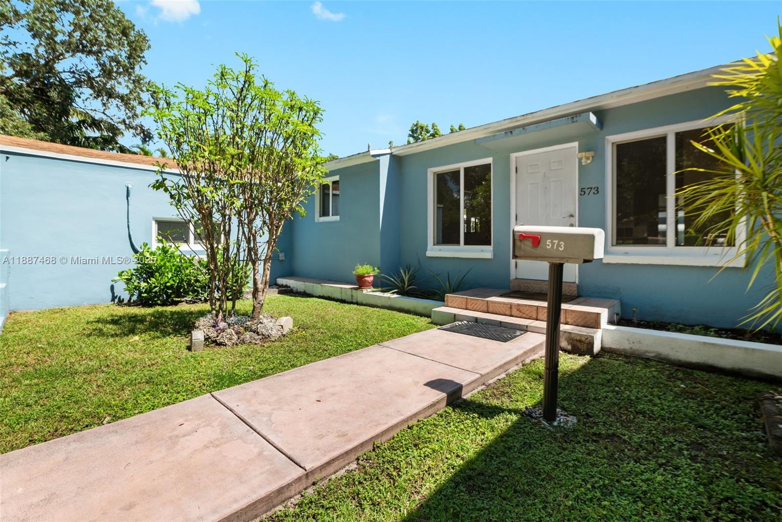 A light blue house features a concrete walkway leading to a front door and mailbox — 573 Palmetto Dr, Miami Springs FL 33166, MIAMI SPRINGS, FL
