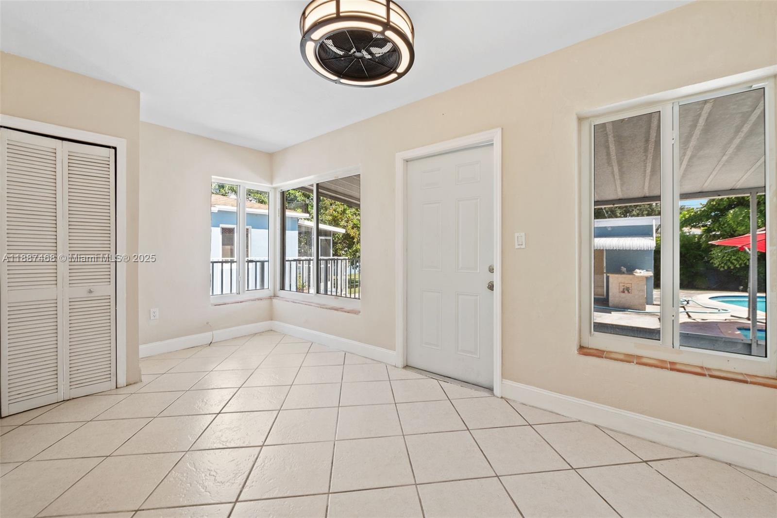 A bright room with tiled floors, a ceiling fan, and windows overlooking a backyard pool — 573 Palmetto Dr, Miami Springs FL 33166, MIAMI SPRINGS, FL