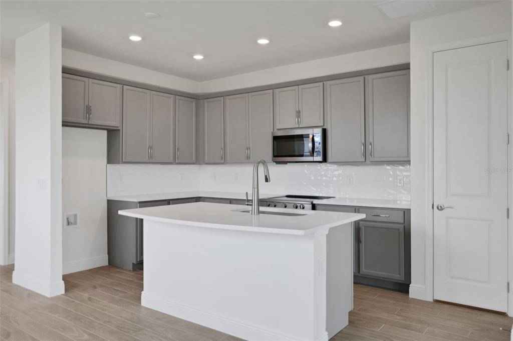 A modern kitchen features gray cabinets, white countertops, a central island, and light wood flooring — 7530 SEA OAK COURT, PARRISH, FL
