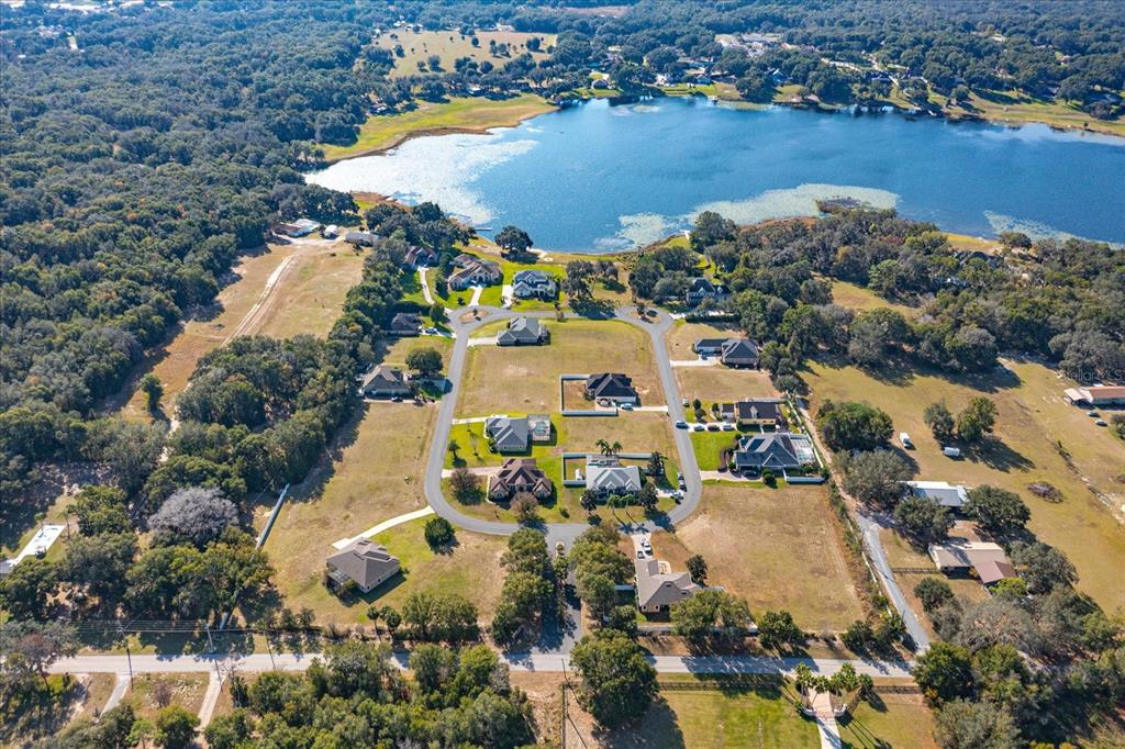 An aerial view shows a residential neighborhood with several houses situated near a large lake — 1002 MYRTLE BREEZES COURT, FRUITLAND PARK, FL