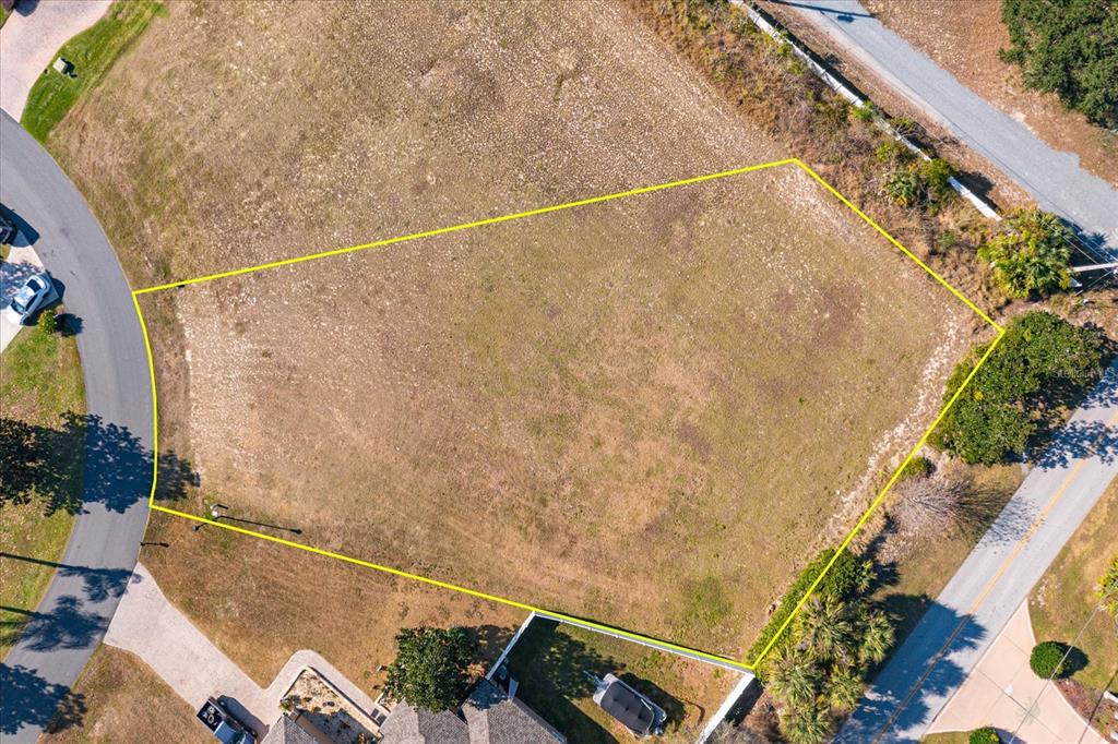 An aerial view shows an empty, irregularly shaped residential lot outlined in yellow — 1002 MYRTLE BREEZES COURT, FRUITLAND PARK, FL