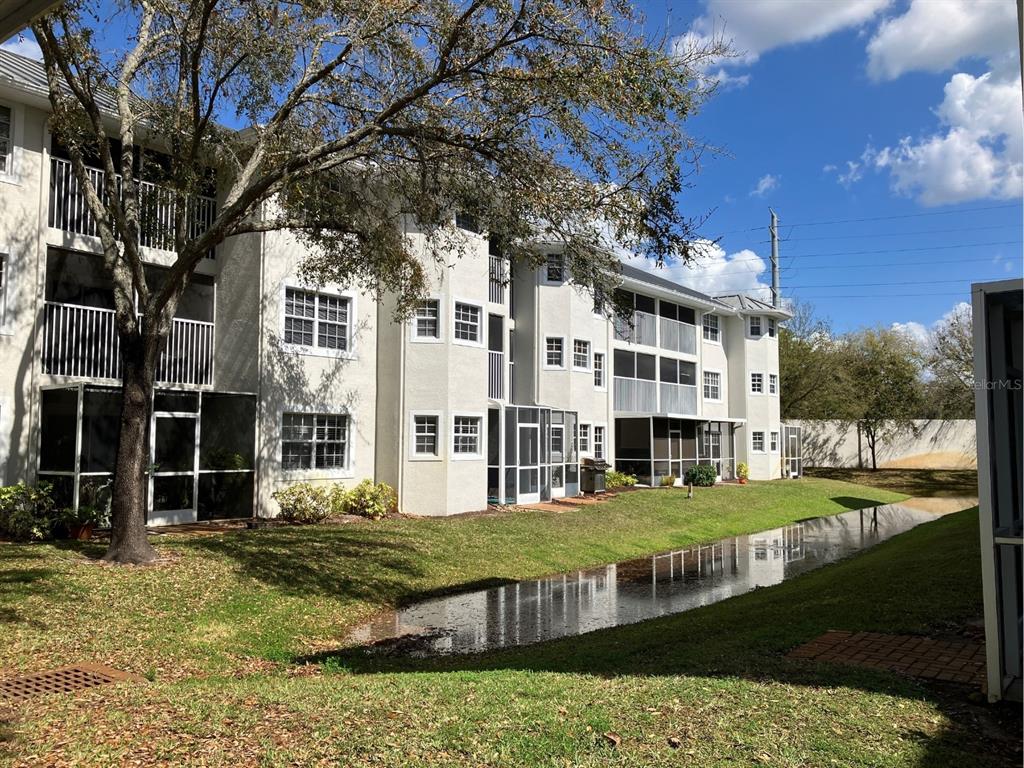 A three-story apartment building with screened balconies sits beside a small pond and lawn — 21146 FOUNTAIN VIEW LANE UNIT 4303, LUTZ, FL