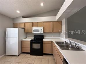 A kitchen features light wood cabinets, black appliances, a white refrigerator, and a double sink — 13403 FAIRWAY GLEN DRIVE UNIT 204, ORLANDO, FL