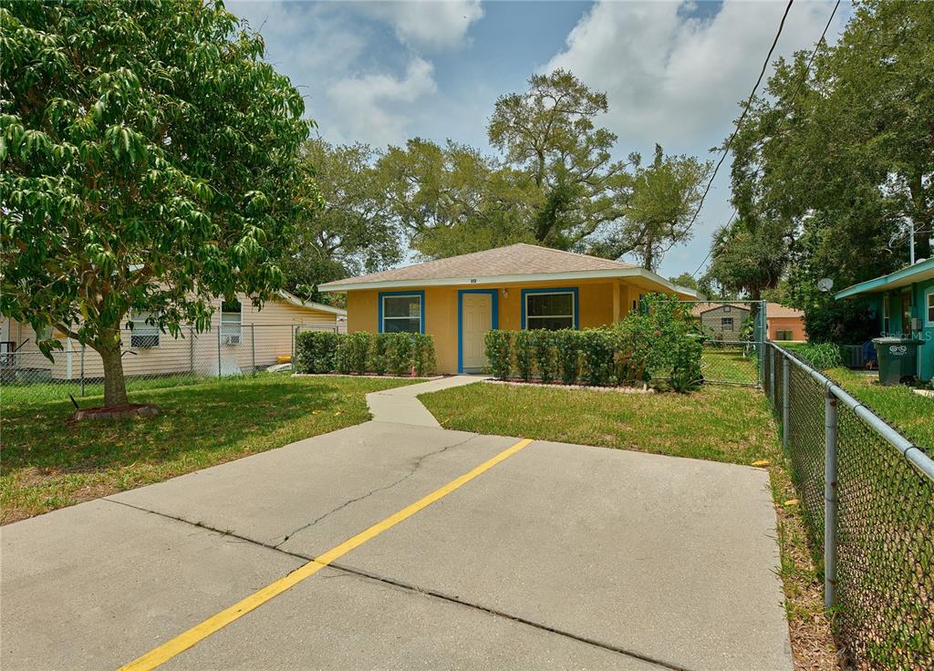 A yellow single-story house with a concrete driveway and a chain-link fence in the front yard — 212 13TH AVENUE W, BRADENTON, FL