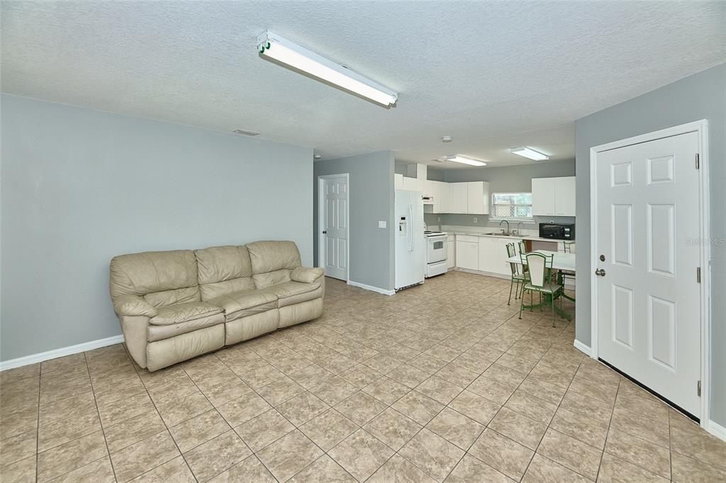 A living room with tile flooring and a beige sofa opens into a white kitchen — 212 13TH AVENUE W, BRADENTON, FL