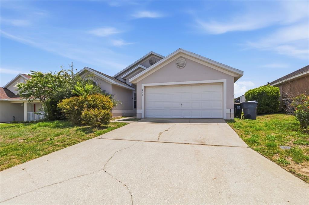 A single-story house with a beige exterior, a two-car garage, and a concrete driveway — 210 PINE CONE DRIVE, DAVENPORT, FL