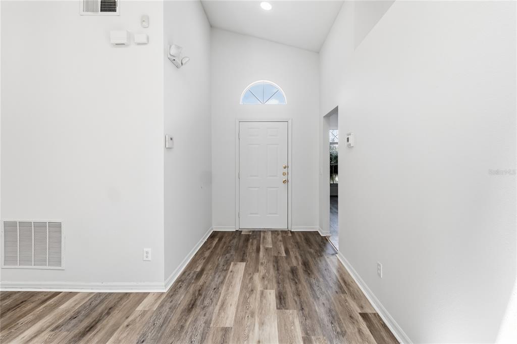 An entryway with white walls, a vaulted ceiling, and wood-look flooring leads to a front door — 210 PINE CONE DRIVE, DAVENPORT, FL