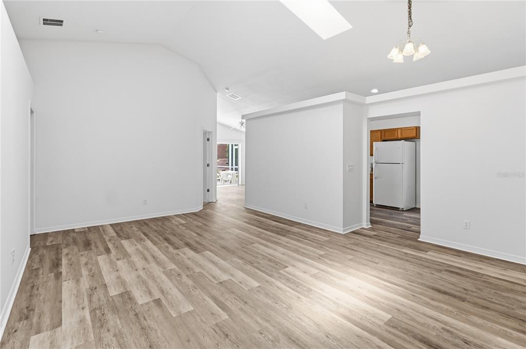 A spacious living room with vaulted ceilings, light wood-look flooring, and an adjacent kitchen area — 210 PINE CONE DRIVE, DAVENPORT, FL