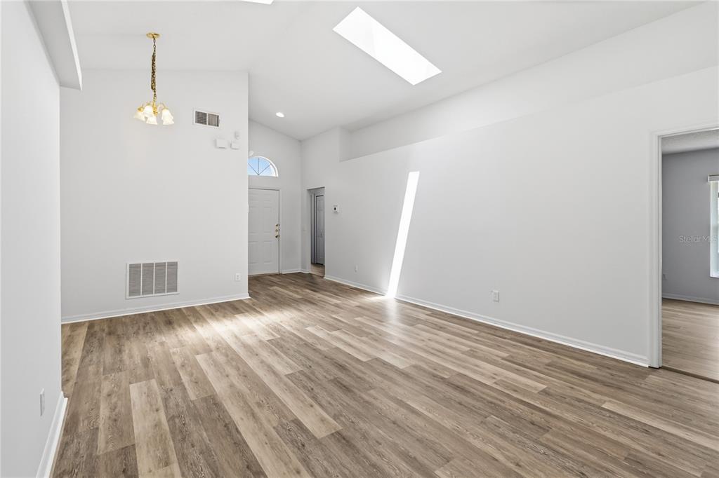 An empty living room with vaulted ceilings, a skylight, and light wood-look flooring — 210 PINE CONE DRIVE, DAVENPORT, FL