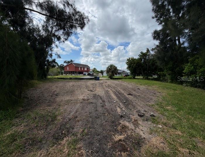 A cleared, dirt-covered vacant lot sits between trees with a red house in the background — 1020 LINDEN ROAD, VENICE, FL