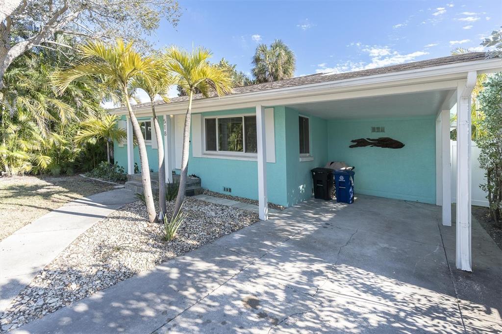 A turquoise single-story house features a concrete driveway, a covered carport, and palm trees — 518 77TH AVENUE, ST PETE BEACH, FL