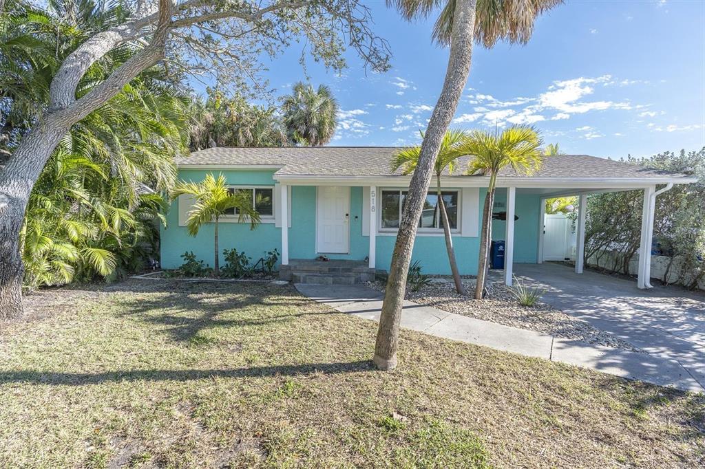 A turquoise single-story house features a front porch, a carport, and surrounding palm trees — 518 77TH AVENUE, ST PETE BEACH, FL