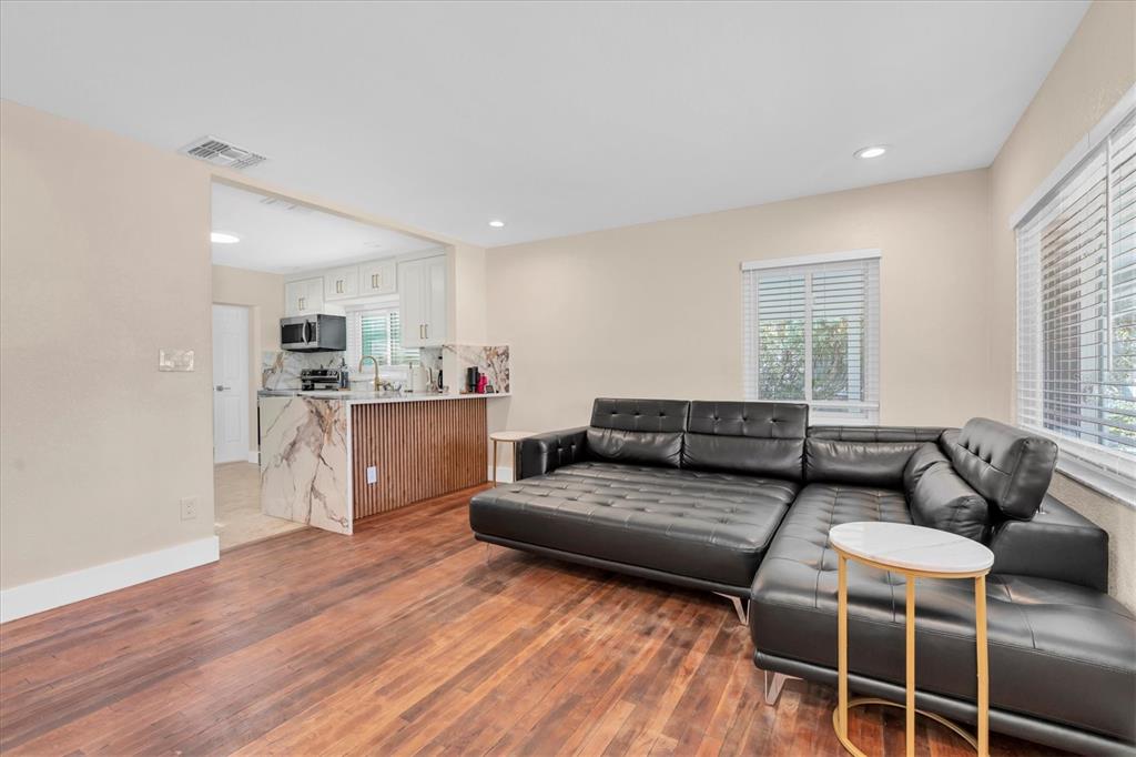 A living room with wood floors, a black leather sectional, and an open kitchen area — 518 77TH AVENUE, ST PETE BEACH, FL