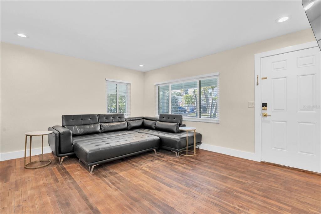 A living room features a black sectional sofa, wood flooring, and a white front door — 518 77TH AVENUE, ST PETE BEACH, FL