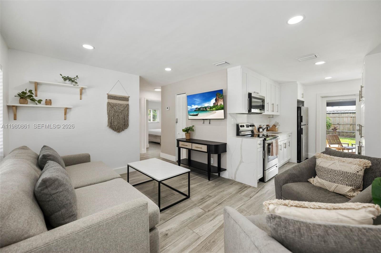 A living room with gray sofas, a white coffee table, and an adjacent kitchen area — 1448 NE 25th Ct, Pompano Beach FL 33064, POMPANO BEACH, FL