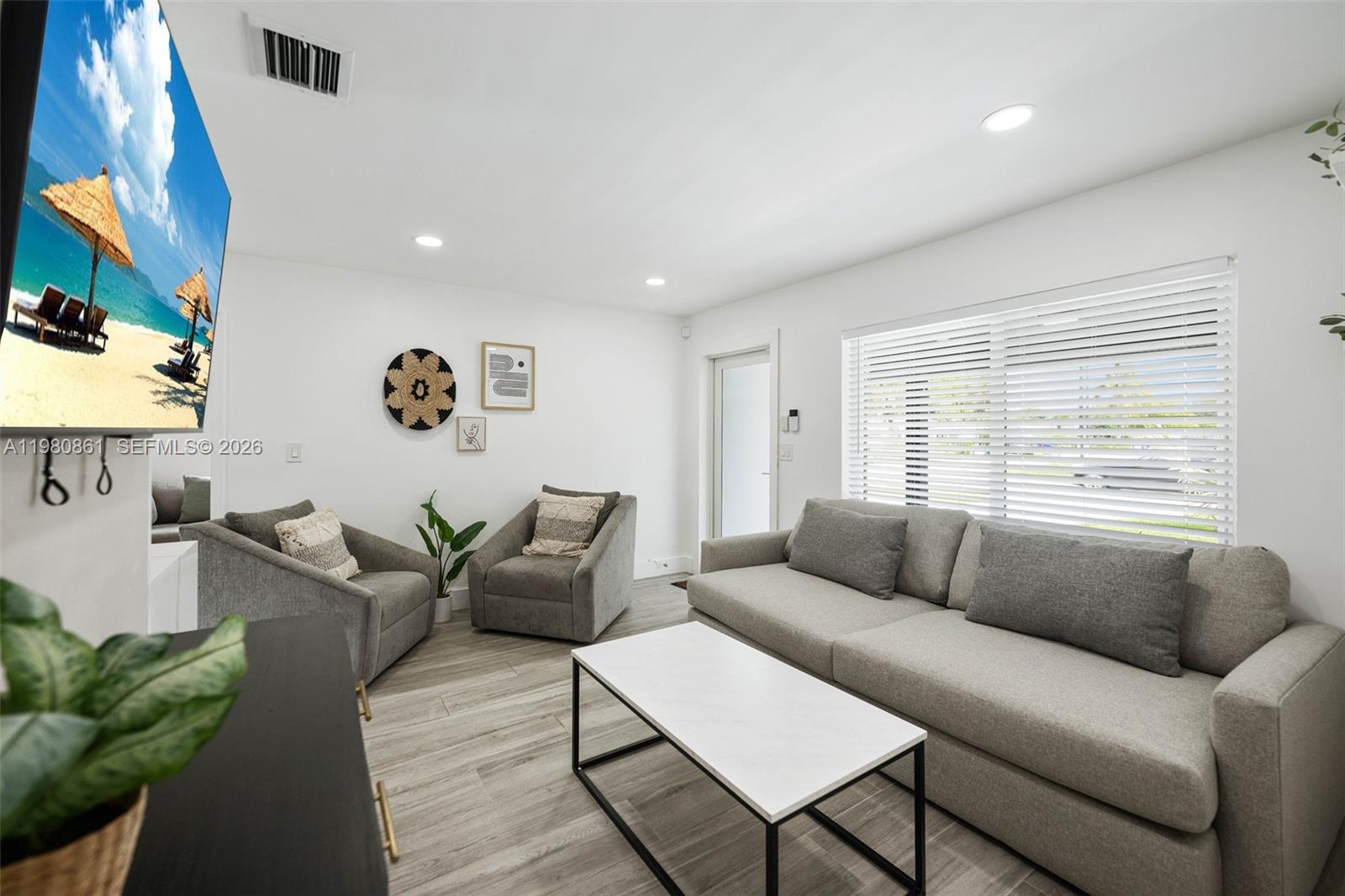 A living room features a gray sofa, two armchairs, a coffee table, and a wall-mounted television — 1448 NE 25th Ct, Pompano Beach FL 33064, POMPANO BEACH, FL