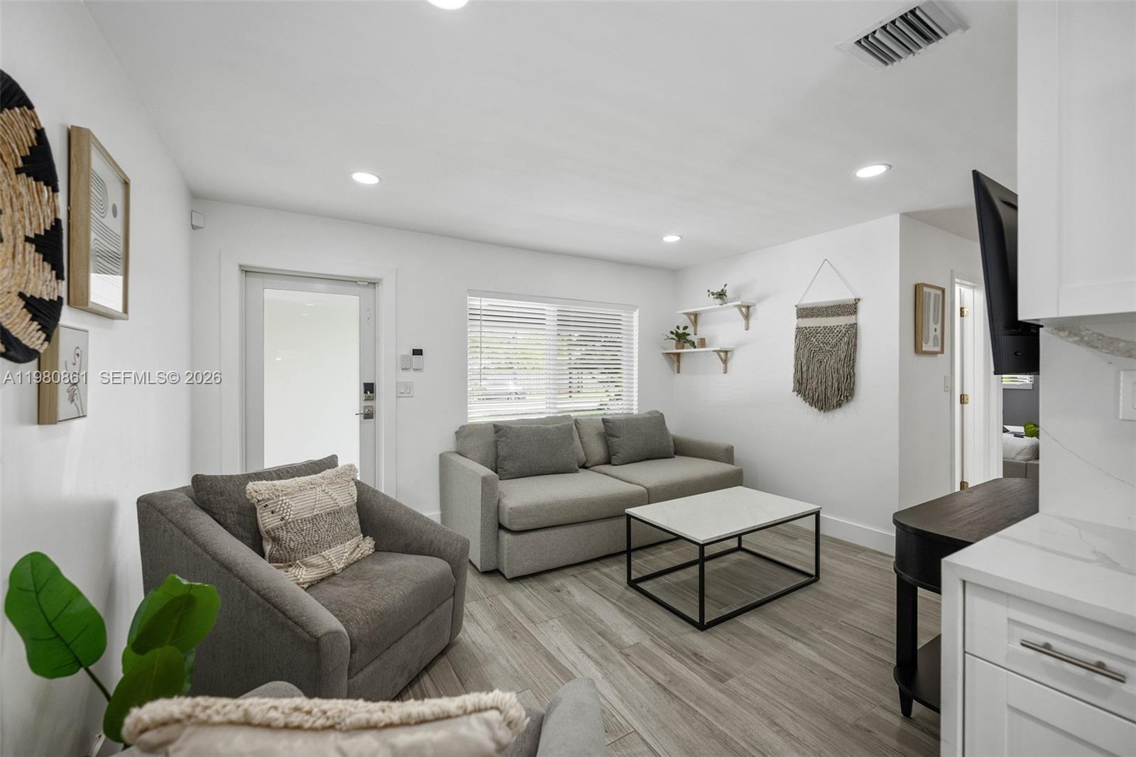 A living room features gray furniture, a marble-topped coffee table, and light wood-look flooring — 1448 NE 25th Ct, Pompano Beach FL 33064, POMPANO BEACH, FL