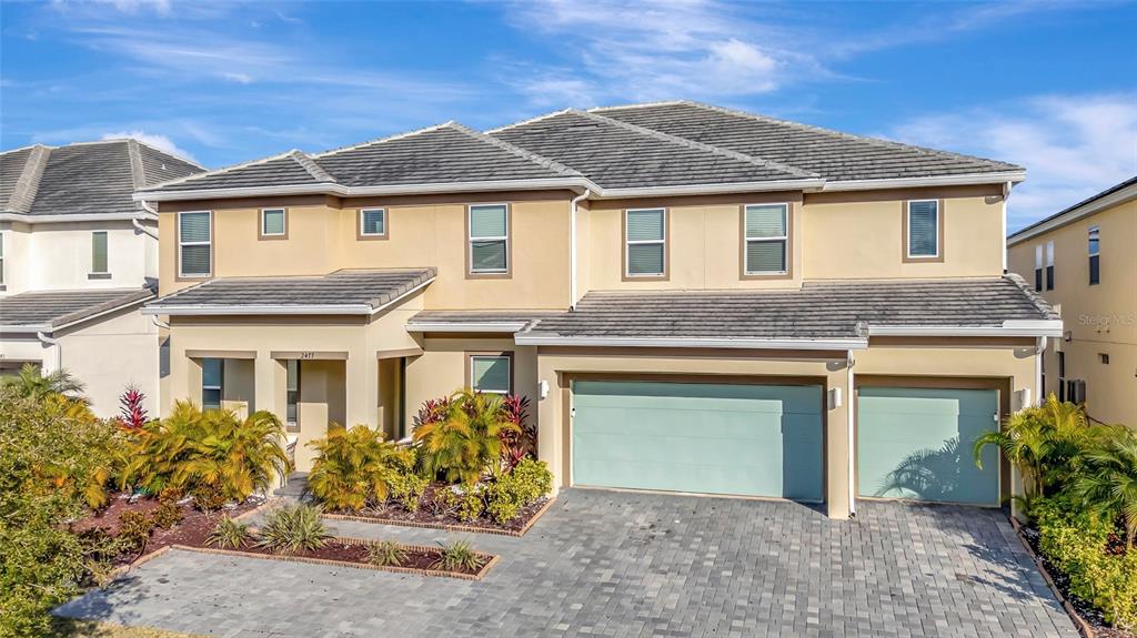 A two-story tan house with a three-car garage and a paved driveway — 2477 SHANTI DRIVE, KISSIMMEE, FL