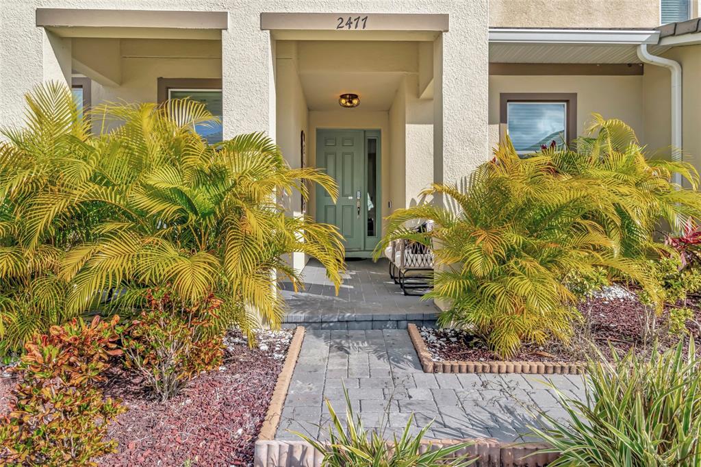 A paved walkway leads to the front entrance of a house with a teal door — 2477 SHANTI DRIVE, KISSIMMEE, FL