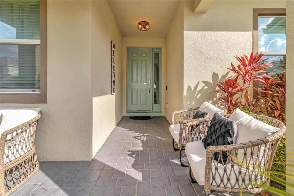 A covered front porch features a light blue door, gray pavers, and two wicker chairs — 2477 SHANTI DRIVE, KISSIMMEE, FL