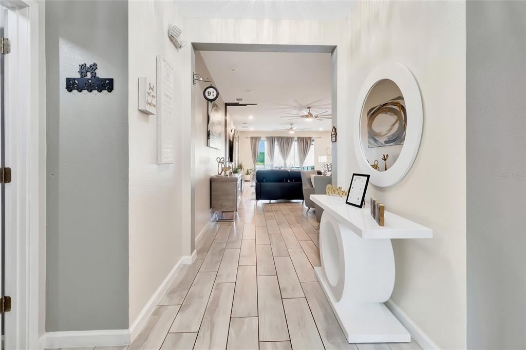 A hallway with light wood-look tile flooring leads into an open-concept living area — 2477 SHANTI DRIVE, KISSIMMEE, FL